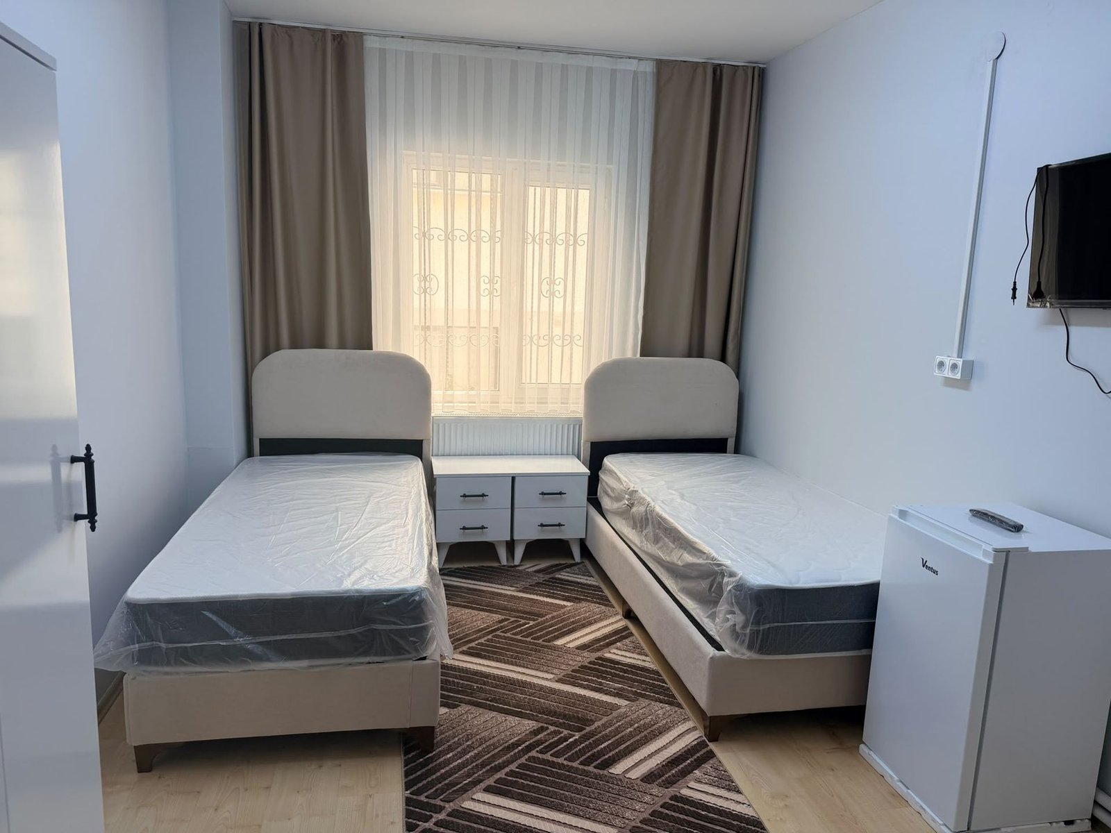 A double room with two beds, study desks, a television and a mini fridge